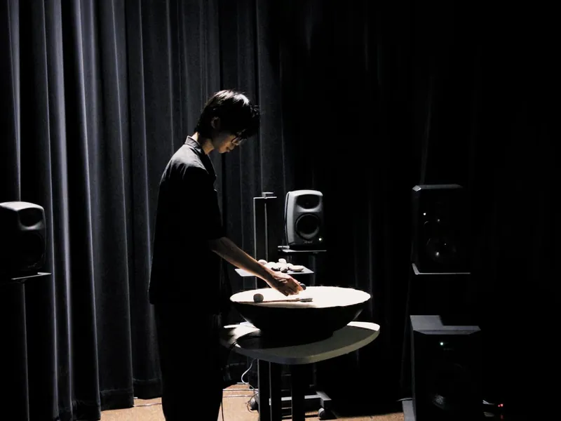 A person standing at SoundMat in the dark media lab, moving stones